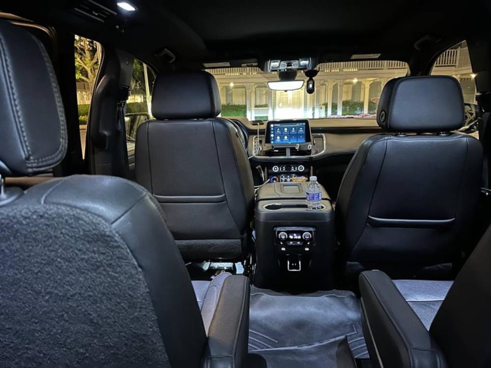 Interior view of a modern SUV from the back seat, showcasing black leather seats and a center console with a water bottle—this is true Olive Luxury Ride comfort, complete with a sleek touchscreen dashboard display.