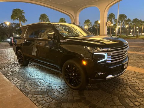 A black SUV offering transportation to MCO Airport is parked on a cobblestone driveway under a canopy at dusk, its headlights aglow and palm trees visible in the background.