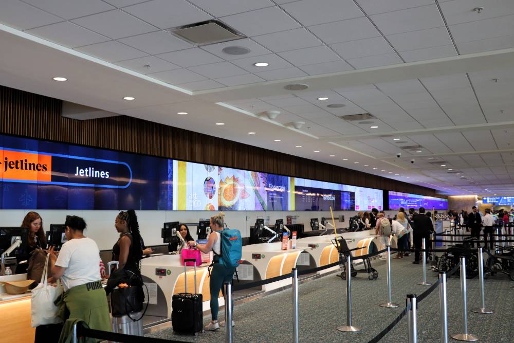 People stand in line and check in luggage at a brightly lit Jetlines counter inside an airport terminal, preparing to connect with Orlando Airport Transportation Services for their onward journey.