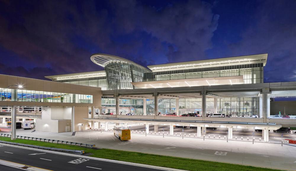 Modern airport terminal at night with illuminated glass and steel architecture, multiple levels for traffic and buses, and a dark sky in the background—ideal for seamless Orlando Airport Transportation Services.