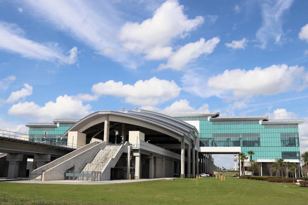 Modern building with glass exterior and large arched entrance, surrounded by grass under a partly cloudy sky—conveniently located with easy transportation to MCO Airport nearby.