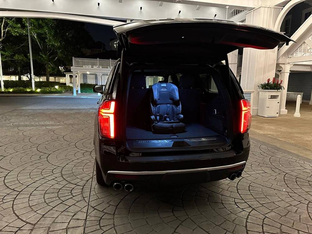 A black SUV with its rear hatch open shows a single car seat installed in the cargo area at night in a well-lit driveway, reflecting the safety and comfort offered by luxury car services in Orlando.