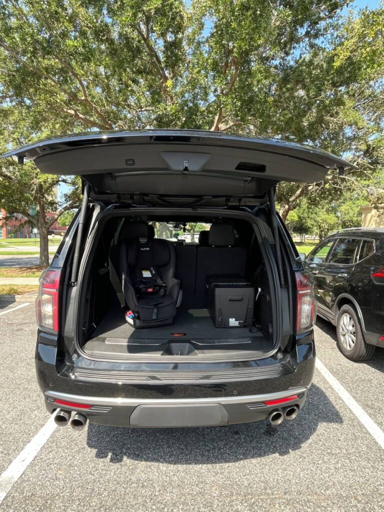 A black SUV from Black Car Service Orlando with the trunk open reveals an installed child car seat and folded third-row seats, parked in a sunny lot with trees in the background.