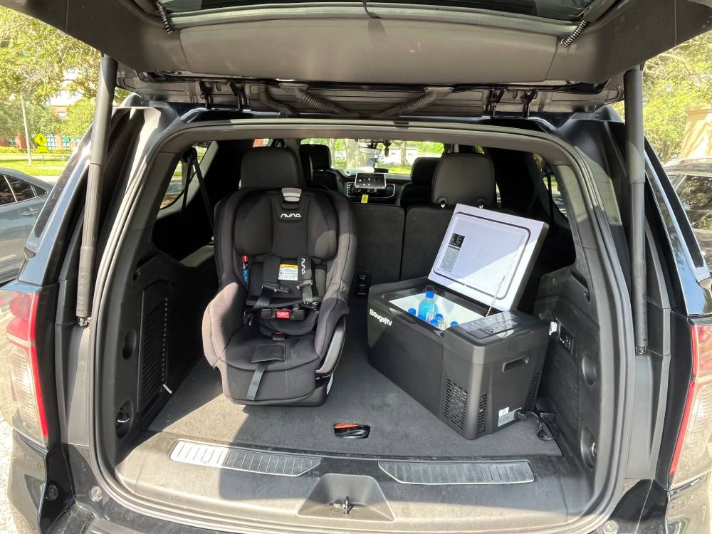 SUV trunk with an installed child's car seat and a portable fridge containing drinks, viewed from the open rear hatch in daylight—perfect for families using Car Service to the Orlando airport.