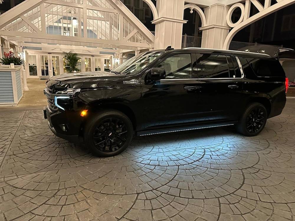 A black SUV from Black Car Service Orlando is parked on a patterned stone driveway at night near a well-lit building with white columns and decorative arches.