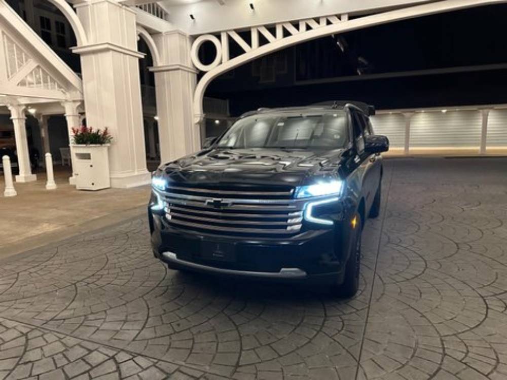 An Olive Luxury Ride—a black Chevrolet SUV with headlights on—is parked on a patterned driveway in front of a well-lit building at night.