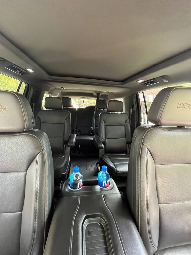 The interior of a large SUV from Black Car Service Orlando features black leather seats, two bottled waters in the center console, and three rows of seating visible.