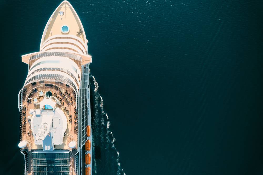 Aerial view of a large cruise ship sailing through calm, dark blue water, ready to welcome guests arriving via transportation from MCO to Port Canaveral.