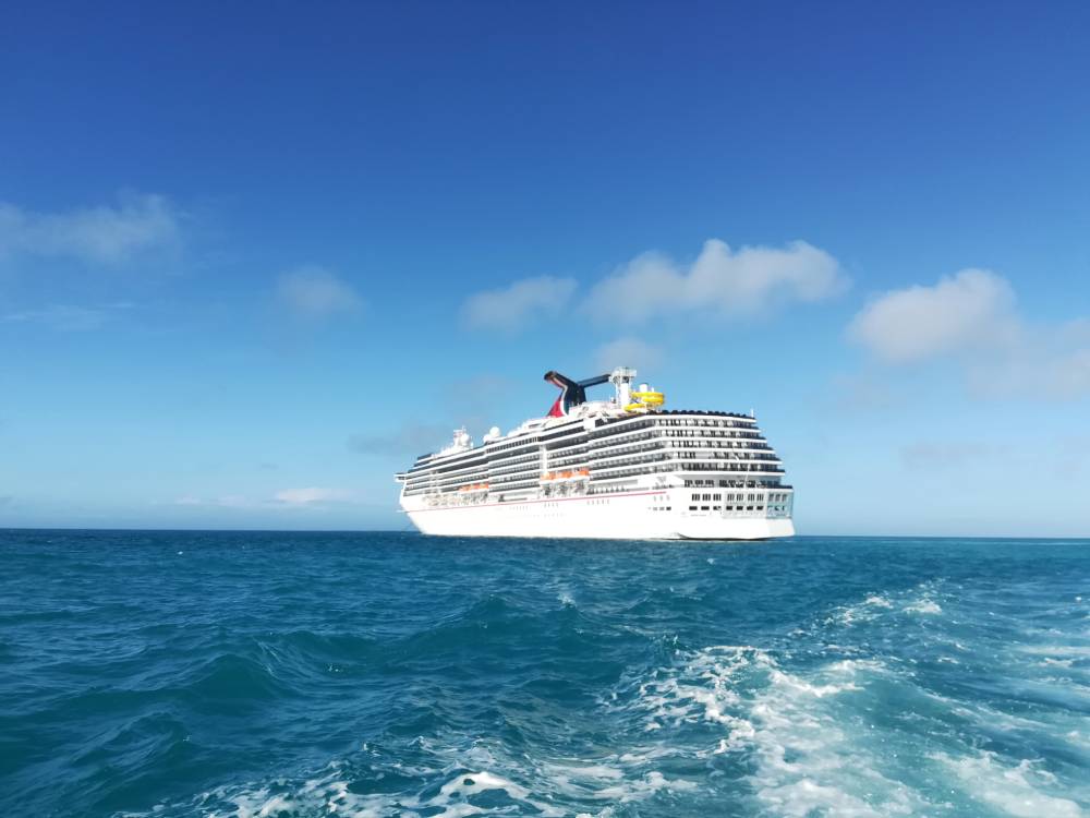 A large white cruise ship sails on calm blue ocean water under a clear sky with a few clouds, ready to welcome passengers arriving by transportation from MCO to Port Canaveral.
